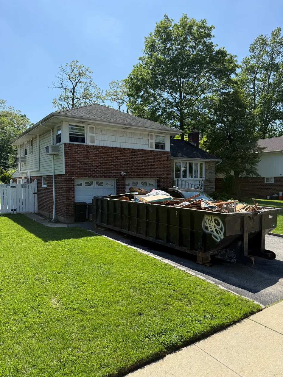 Pyrate Dumpsters roll-off dumpster loaded with cleanout debris on a residential driveway in Carle Place, NY