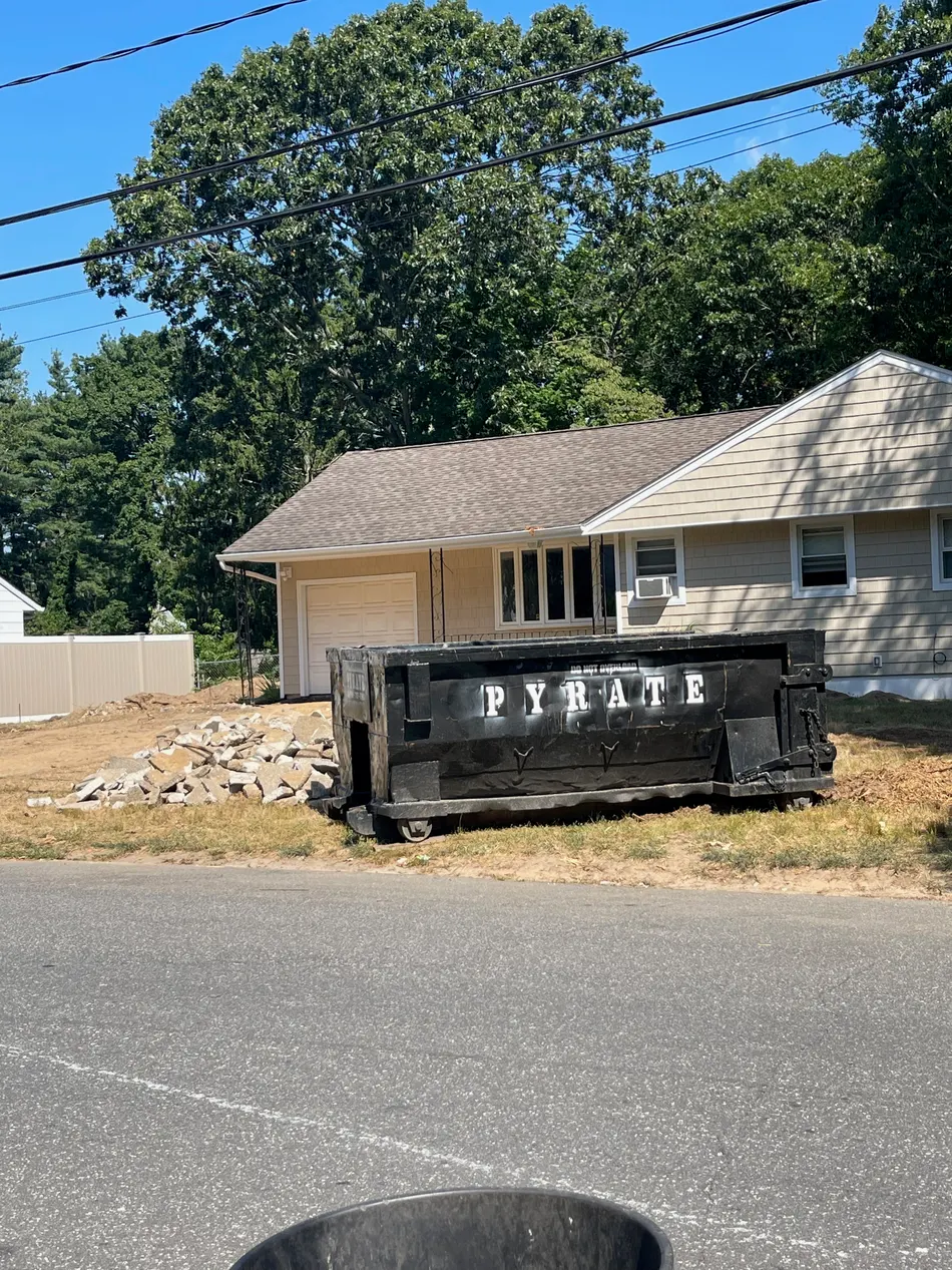 Pyrate Dumpsters branded roll-off dumpster with a concrete debris pile at a home in New Cassel, NY